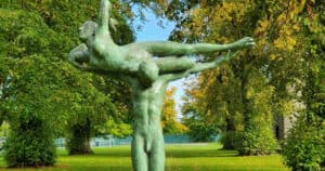 Bronze sculpture of a human figure carrying another figure, set in a lush green park at The Kildare Gallery.