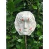 Ceramic face art sculpture surrounded by lush green leaves at The Kildare Gallery, showcasing contemporary Irish artistic design.
