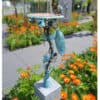 Antique metal sculpture of a bird perched on a stand, surrounded by vibrant flowers.