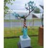 Blue metal sculpture of a bird perched on a tree branch in outdoor garden.