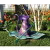 Colorful mouse sculpture holding a rake in a garden setting with vibrant flowers.