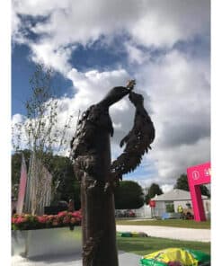Dark bronze sculpture of a woman holding a small bird against a partly cloudy sky at The Kildare Gallery in Ireland.