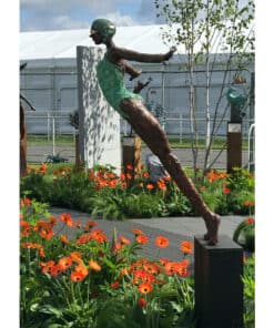 Modern outdoor sculpture of a woman in motion, surrounded by vibrant flowers and garden art.