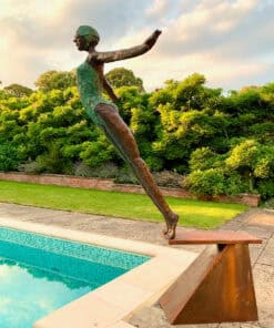 Bronze sculpture of a woman balancing on a plank by a pool at The Kildare Gallery, surrounded by lush greenery.