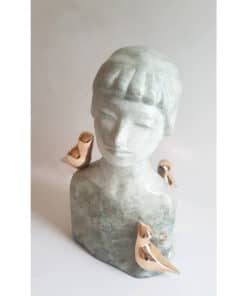 Stone bust sculpture of a young girl's head with metallic bird accents on shoulders and chest.