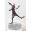 Rustic bronze bunny sculpture dancing on a stone, vibrant art piece displayed at The Kildare Gallery.