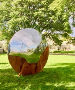 Reflective metallic sphere art installation in Kildare Garden, surrounded by lush greenery and trees.