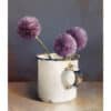 Vase with three purple allium flowers on a neutral background.