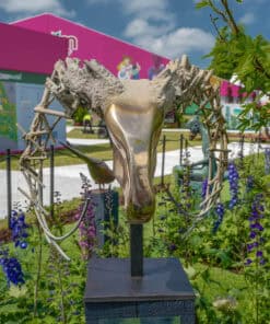 Bronze and concrete abstract sculpture at The Kildare Gallery outdoor exhibition, surrounded by colourful flowers and green foliage.