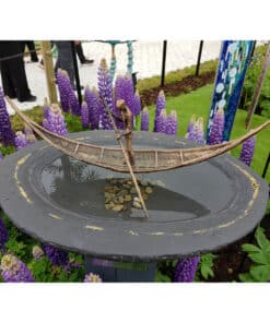 Bronze boat sculpture with a figure paddling, surrounded by purple lupine flowers at The Kildare Gallery.