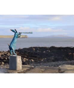 Blue hare sculpture looking through a telescope by the coast.