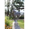 Elegant outdoor metal goat sculpture on stone plinth in garden setting.