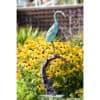 Whimsical metal heron sculpture amid vibrant yellow flowers in a garden.