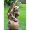 Ancient stone gargoyle sculpture of a winged mythical creature in a lush garden setting.