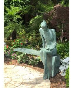 Serene garden sculpture of a woman reading, surrounded by lush greenery and colourful flowers.