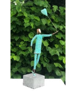 Colourful abstract sculpture of a woman holding a heart-shaped balloon in front of green foliage.