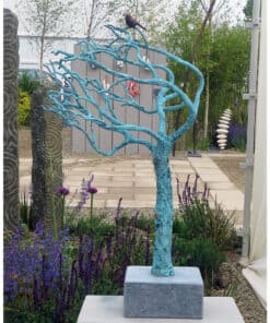 Vibrant blue abstract sculpture of a tree with branches, displayed outdoors at The Kildare Gallery, surrounded by plants and garden art.
