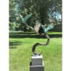 Metal sculpture of two abstract birds with turquoise patina, set outdoors on a sunny day at The Kildare Gallery.