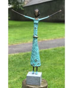 Handmade metal sculpture of a joyful woman with arms raised, outdoor garden setting.