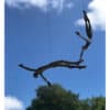 Ancient metal sculpture of a human figure hanging from a tree branch against blue sky.