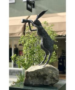 Rustic black metal hare sculpture with a telescope, displayed outdoors at The Kildare Gallery.
