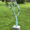 Vibrant outdoor sculpture of a tree with birds, displayed on a grey pedestal at The Kildare Gallery.