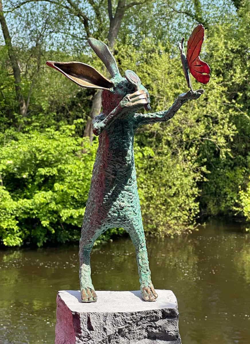 Rabbit sculpture holding a red butterfly in a natural outdoor setting.