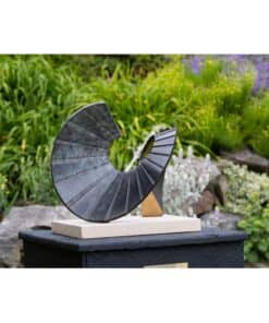 Metal spiral sculpture in a lush garden setting.