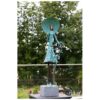 Delicate bronze sculpture of a woman with umbrella, set outdoors amidst lush trees.