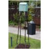 Rustic birdhouse sculpture on tall wooden leg stands in garden sculpture display.