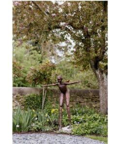 Bronze sculpture of a young child with outstretched arms in a lush garden.