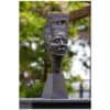 Contemporary bronze sculpture of a woman's face with a textured headpiece outdoors.