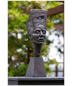 Contemporary bronze sculpture of a woman's face with a textured headpiece outdoors.