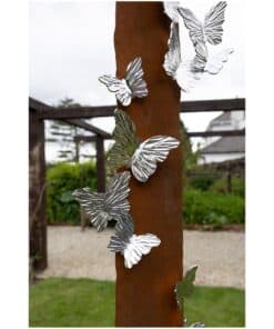 Shiny metal butterfly sculptures on a rusty metal pole in outdoor garden art installation.