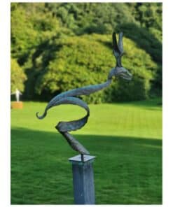 Metal bird sculpture on a pedestal in a lush garden setting.