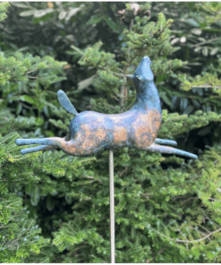 Weathered metal horse garden ornament on stake amid lush green foliage.