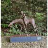 Rusty metal sculpture of a woman riding a dinosaur, outdoor garden setting.