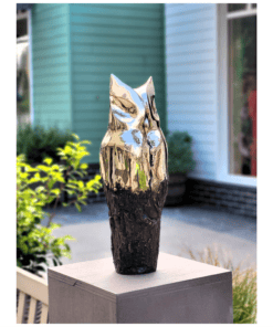 Polished silver owl sculpture on wooden base outside art gallery.