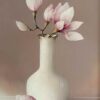 Magnolia flowers in a white ceramic vase on neutral background.